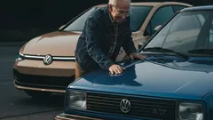 Mies vanhan sinisen Volkswagenin ja uuden Volkswagenin vieressä kadulla